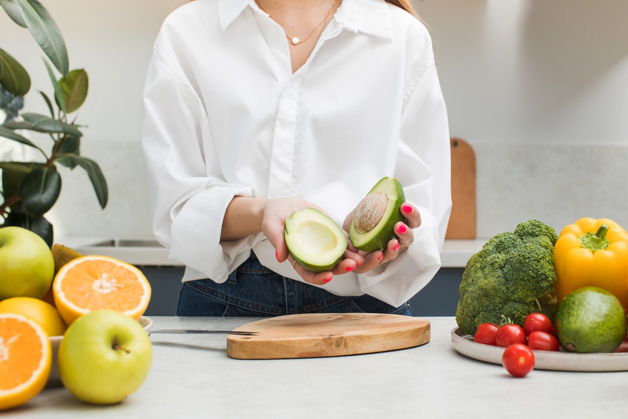 a woman cut a ripe avocado and holds two halves in her hands vegetarianism